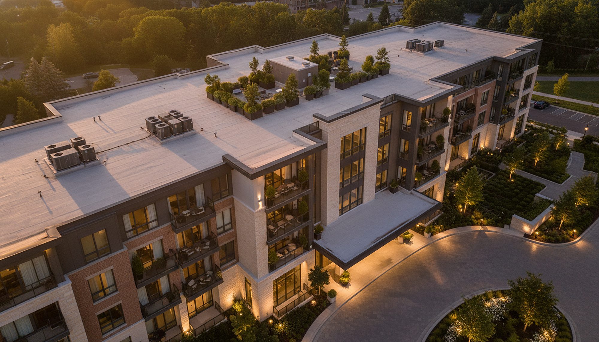 Drone view of the same luxury apartment building's roof, entry canopy and courtyard at golden hour, used as a fictional example